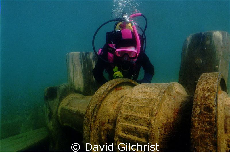 Young diver examines the windlass of the Schooner 'Sweeps... by David Gilchrist 
