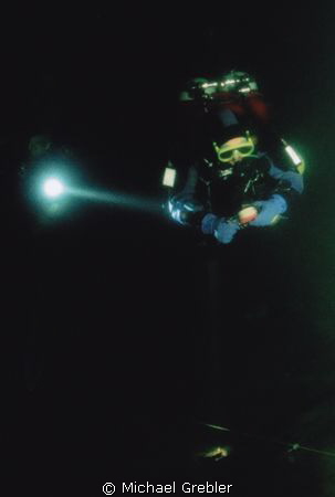 Divers working together in the intense darkness of a floo... by Michael Grebler 