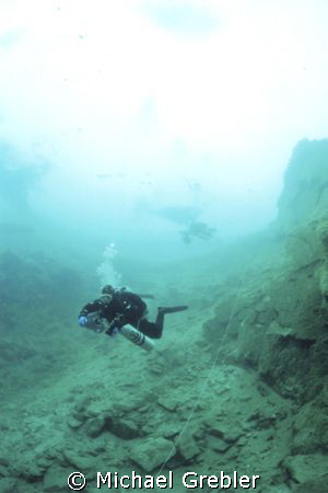Divers descend a rock fall following a cave line under th... by Michael Grebler 