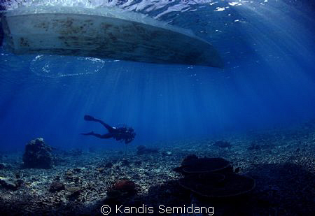 A diver passing under a boat by Kandis Semidang 
