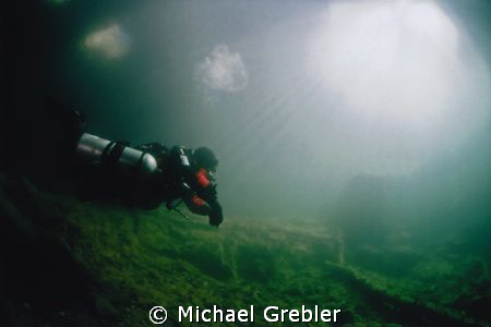 A diver in side-mount gear returns to the warm sunlit ent... by Michael Grebler 