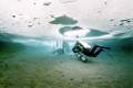 Ice divers, using cave dive techniques, proceeding to the exit hole in the shallows of Morrison Quarry, Quebec. Nikonos V, 12mm Sea & Sea lens, manual exposure. Natural light through the ice, photo not altered. 