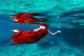 She is swimming in the sea with red dress and fresh water on the top side in the sea.